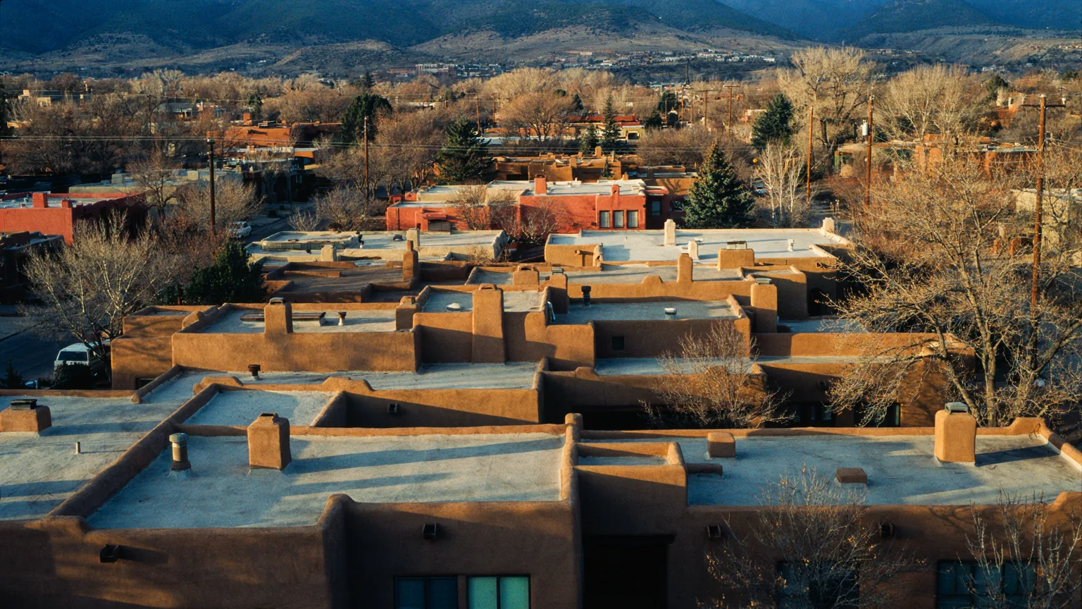 Flat-roofed adobe homes stepping across a Santa Fe neighbourhood at evening.