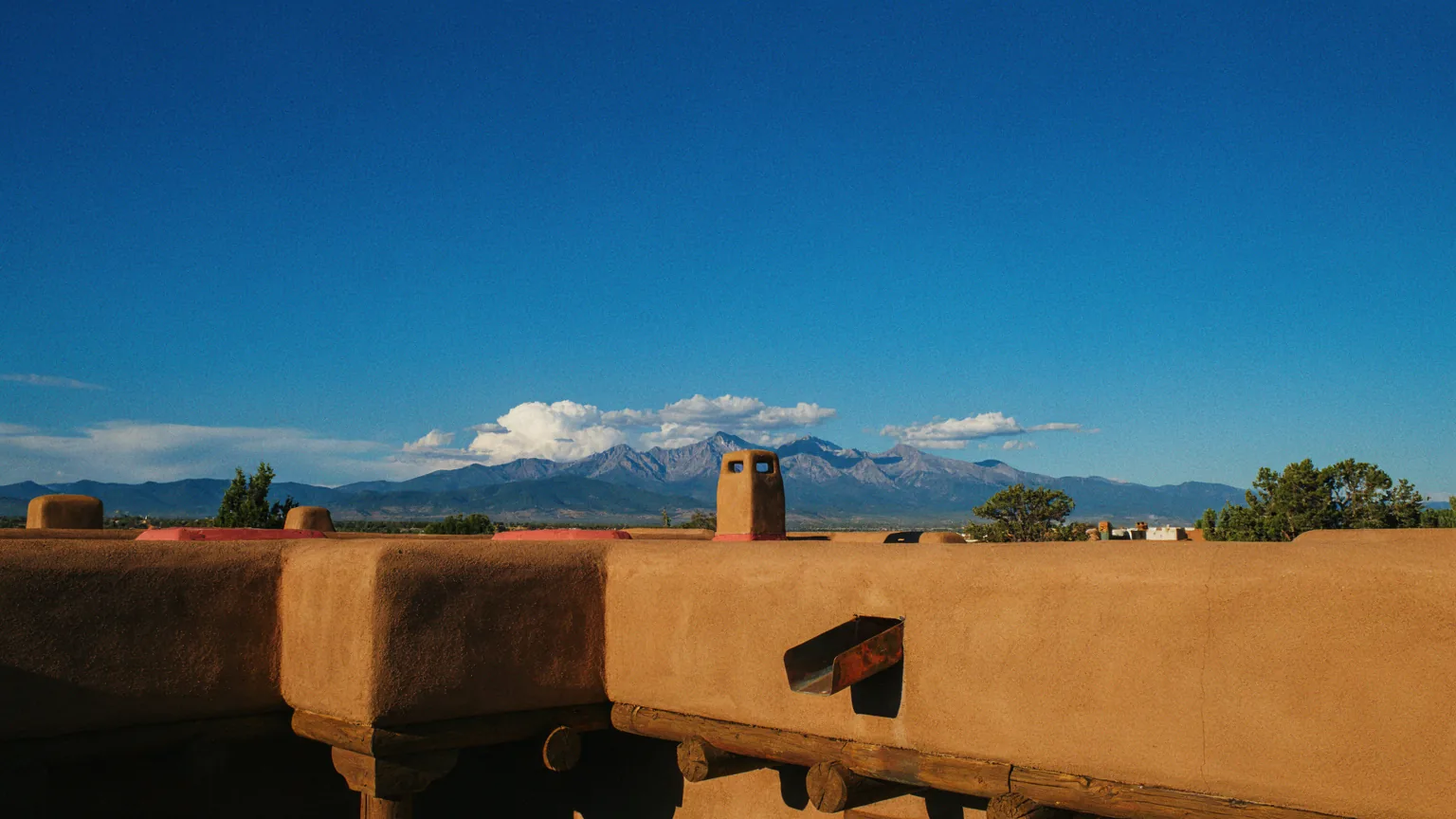 A Santa Fe adobe rooftop at golden hour, showing the flat roof, parapet walls and a copper canale.