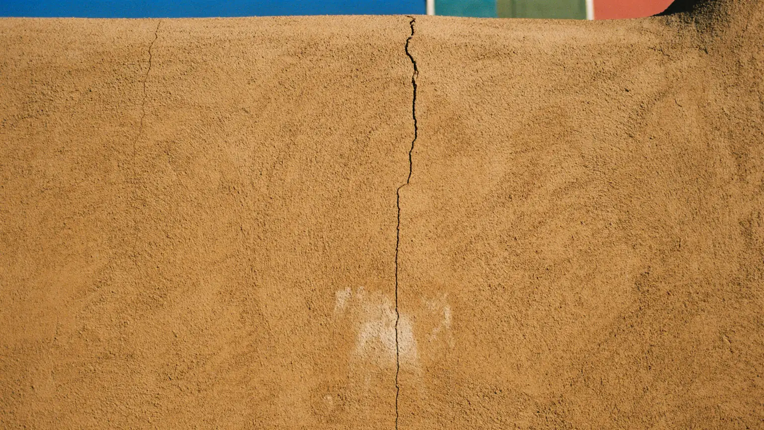 Cracked stucco on an adobe parapet wall, with a prominent vertical crack and efflorescence.